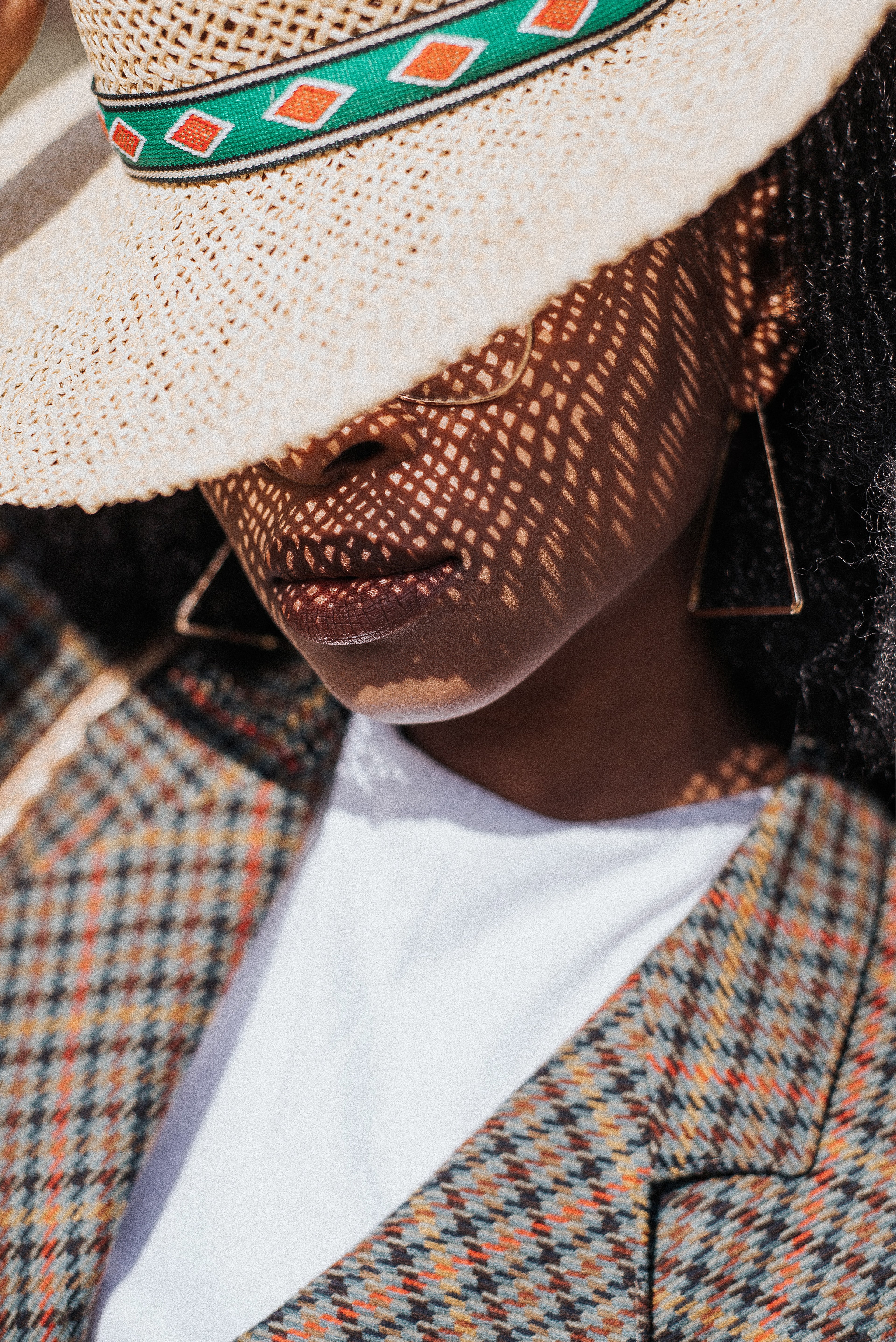 Person wearing a straw hat with a patterned band, plaid coat, and white shirt.