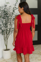 Woman wearing a red dress with bow straps in an indoor setting.