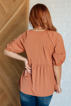 Woman wearing a brown blouse with a white brick wall background