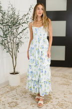 Woman wearing a floral dress standing indoors with a plant in the background