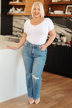 Woman in a white top and blue jeans standing in a kitchen.