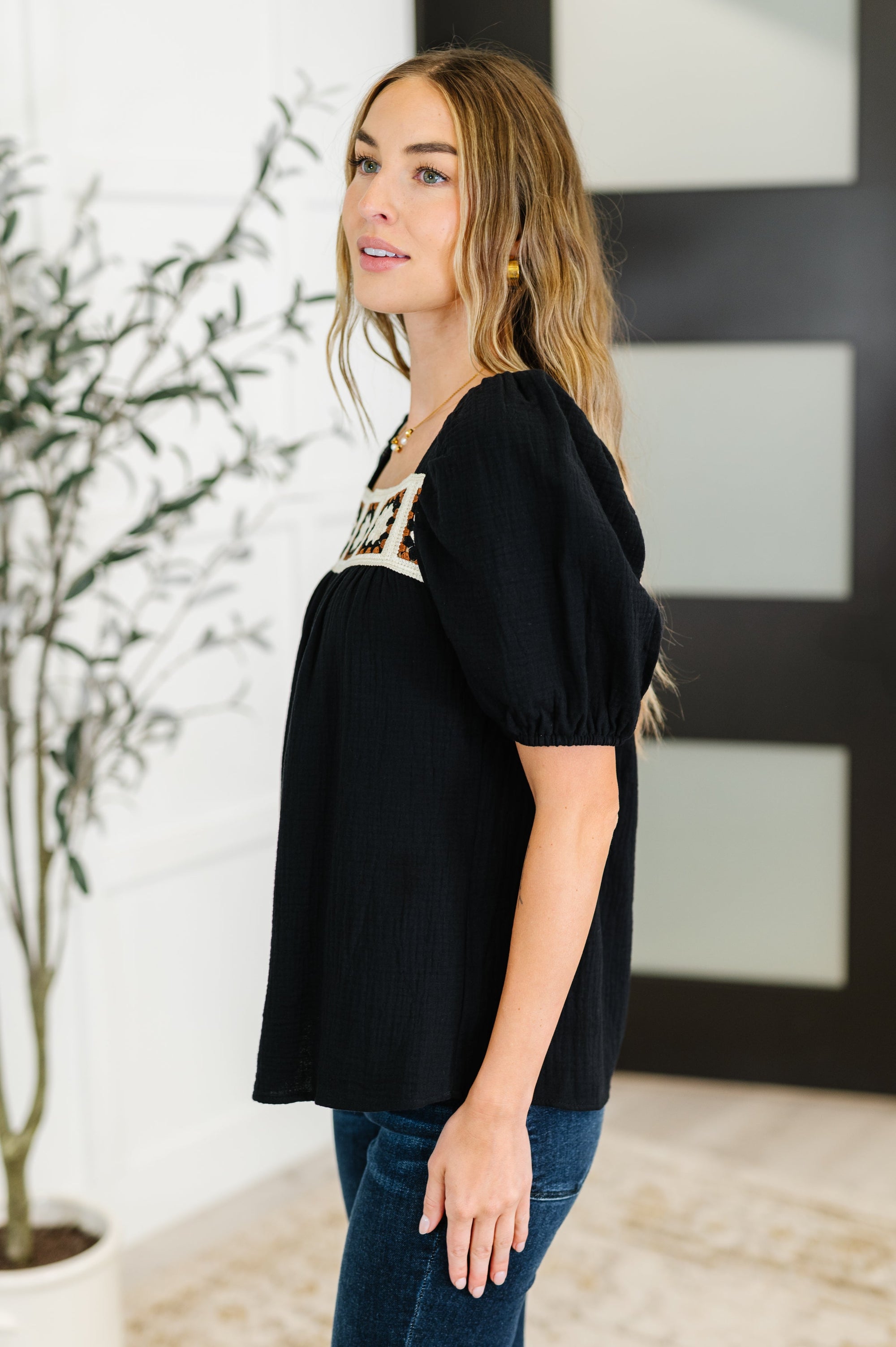 Woman wearing a black top with text and blue jeans indoors