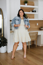 Woman in a white dress and denim jacket standing in a home interior.