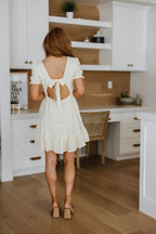 Woman in a white dress with an open back standing in a kitchen.