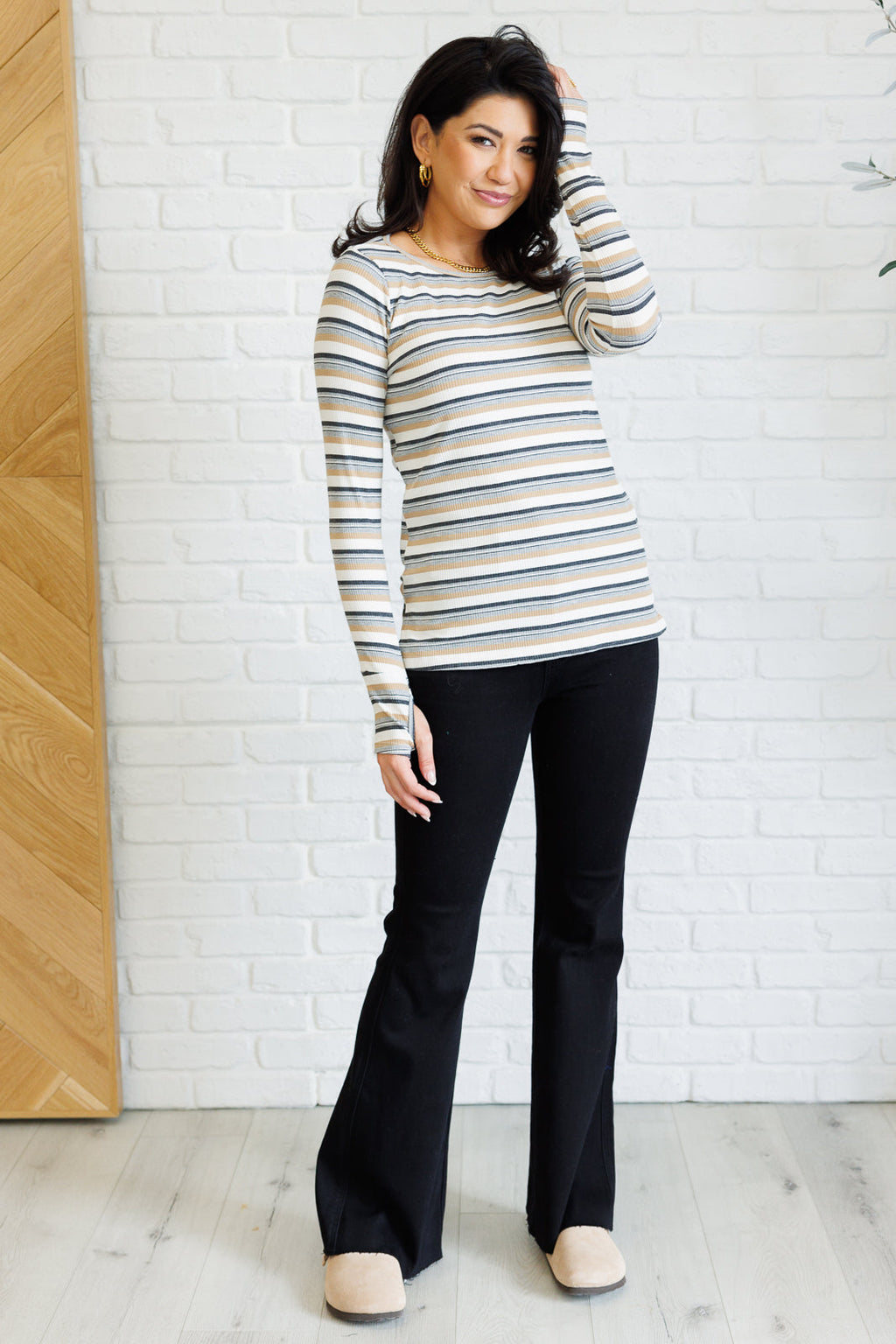 Woman wearing a striped sweater and black pants against a white brick wall.