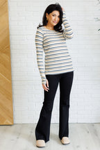 Woman wearing a striped sweater and black pants against a white brick wall.