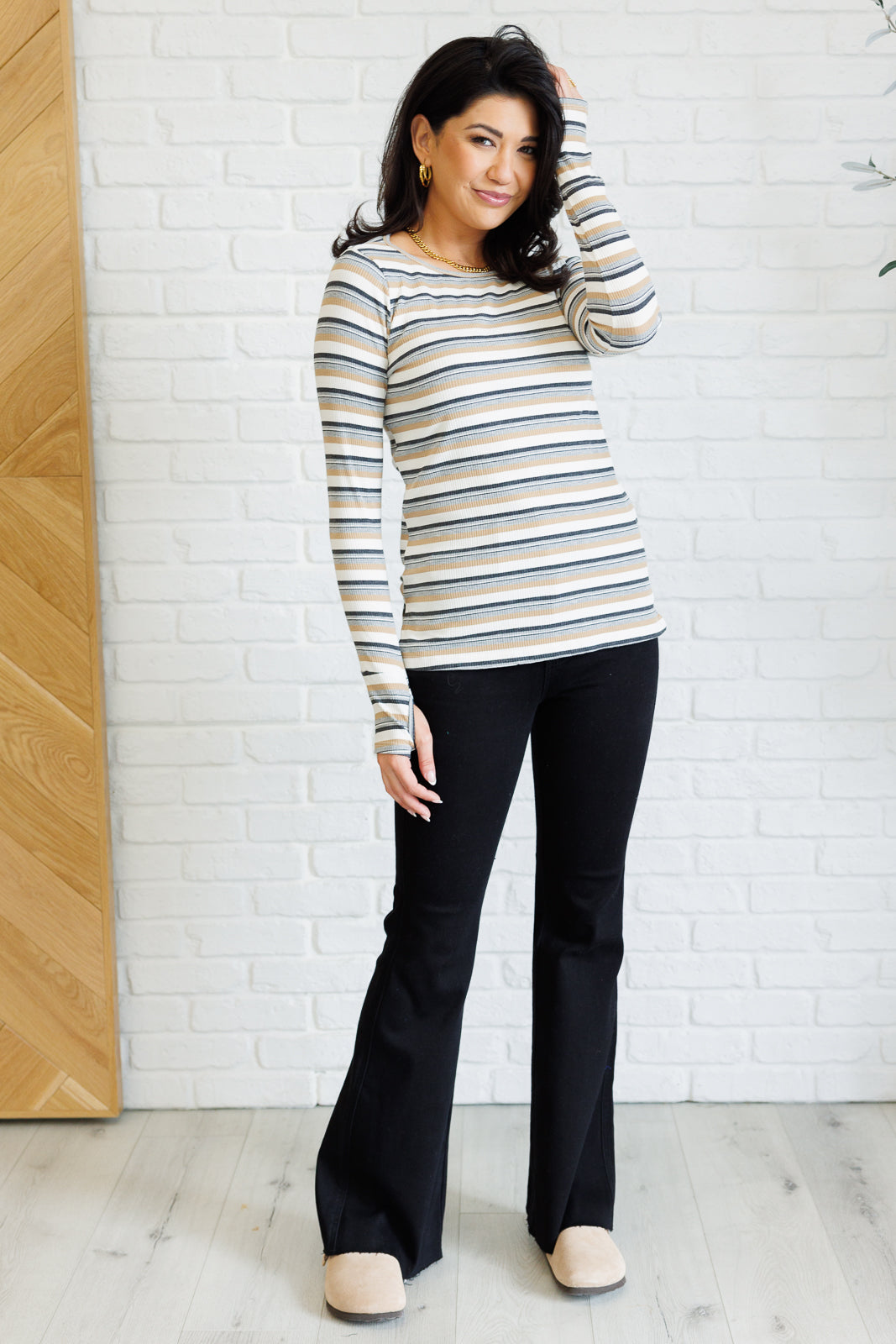 Woman wearing a striped sweater and black pants against a white brick wall.