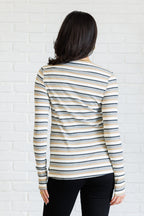 Woman wearing a striped long-sleeve top against a white brick wall.