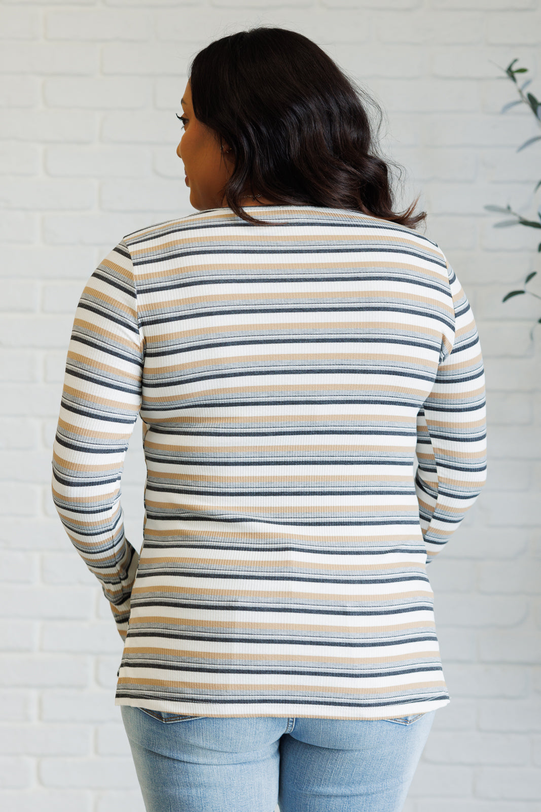 Woman wearing a striped long-sleeve top against a white brick wall.