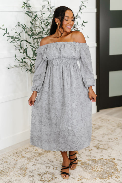 Woman wearing a gray off-shoulder dress standing indoors with decorative elements.