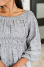 Close-up of a person wearing a light gray textured dress with long sleeves.