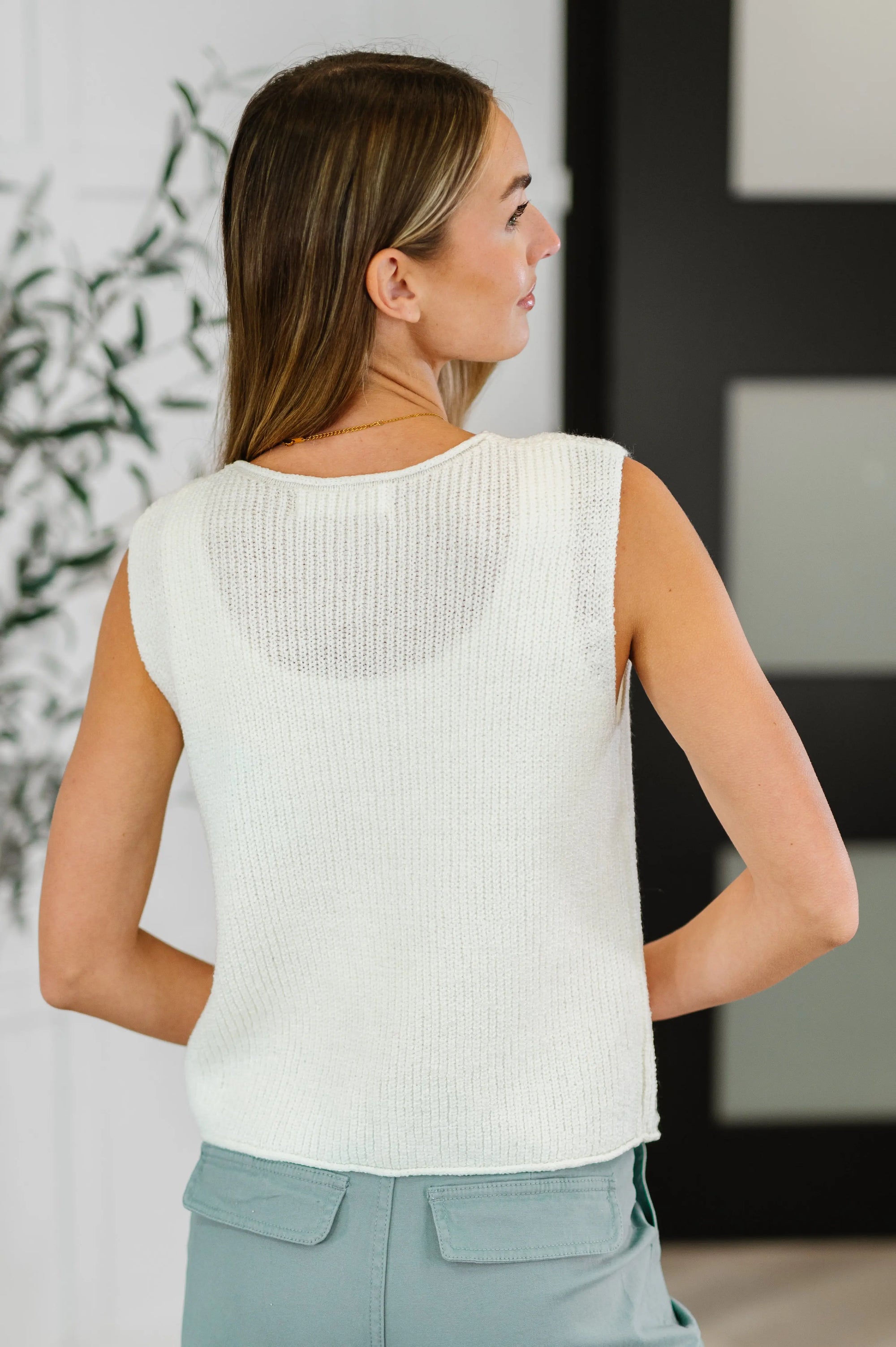 Woman wearing a white sleeveless top and light blue pants in an indoor setting.