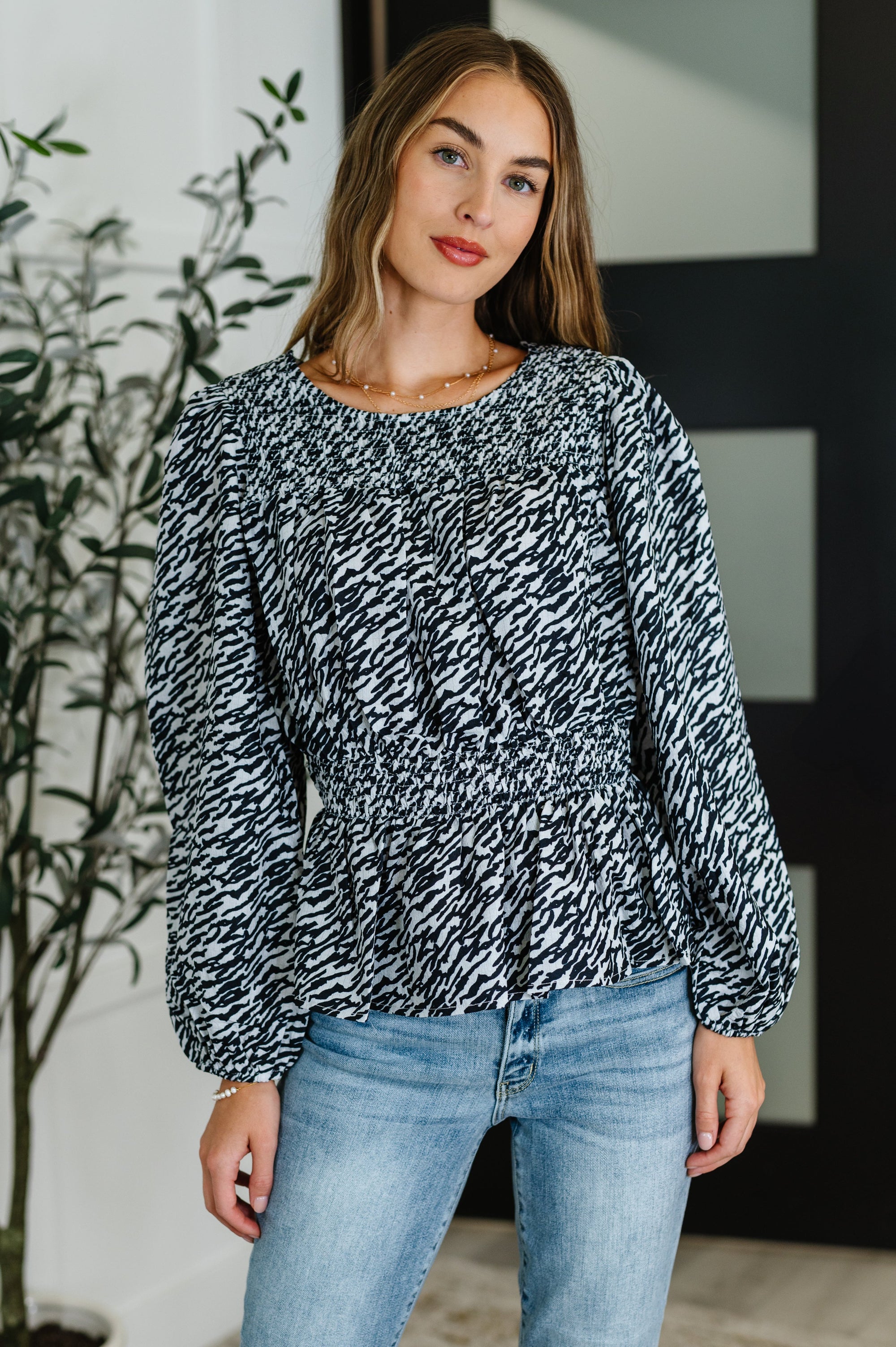Woman wearing a black and white patterned blouse and blue jeans indoors.