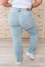 Person wearing light blue jeans and a white shirt against a brick wall.