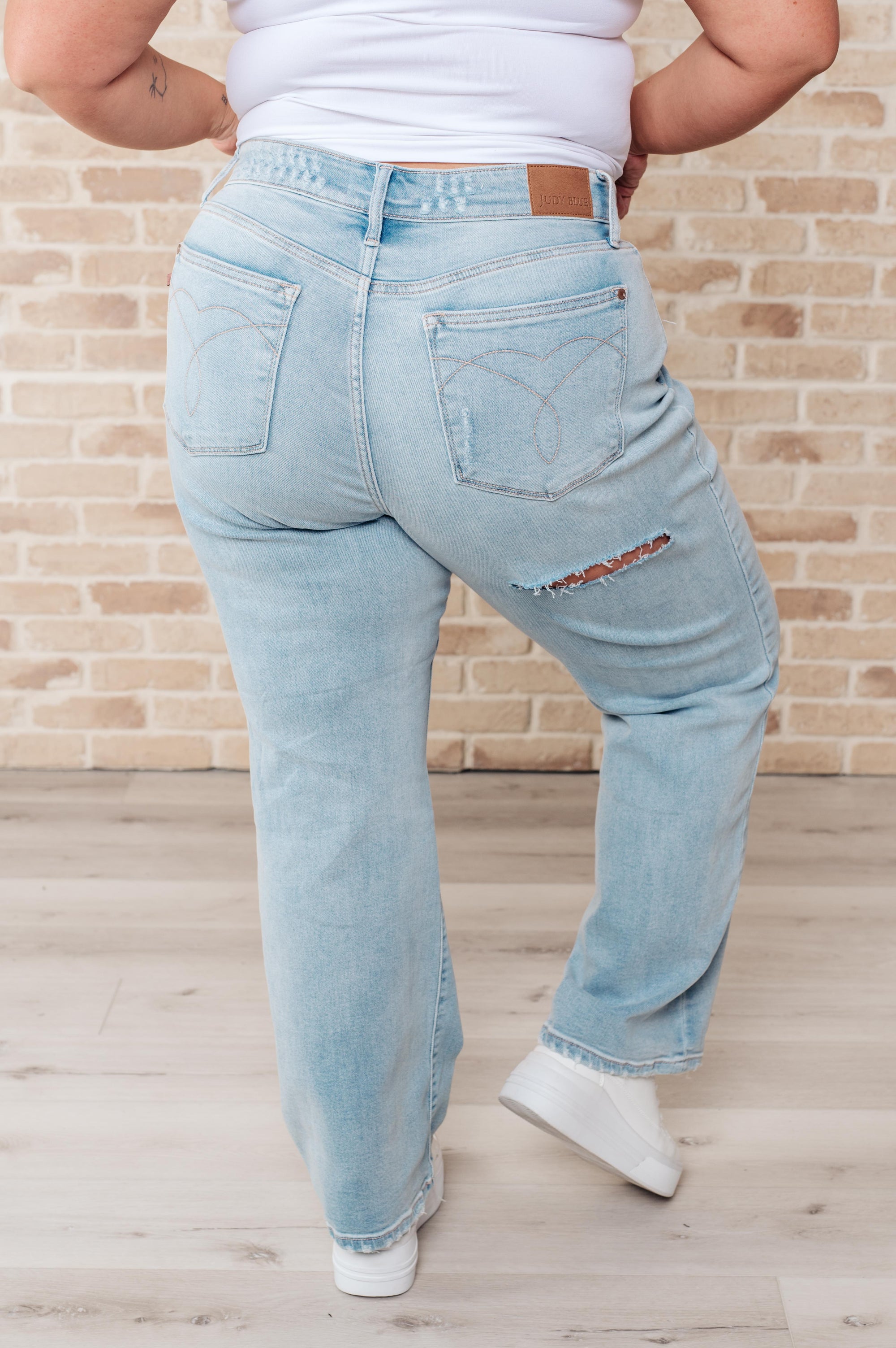 Person wearing light blue jeans and a white shirt against a brick wall.