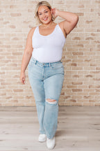 Woman wearing a white tank top and light blue jeans against a brick wall.