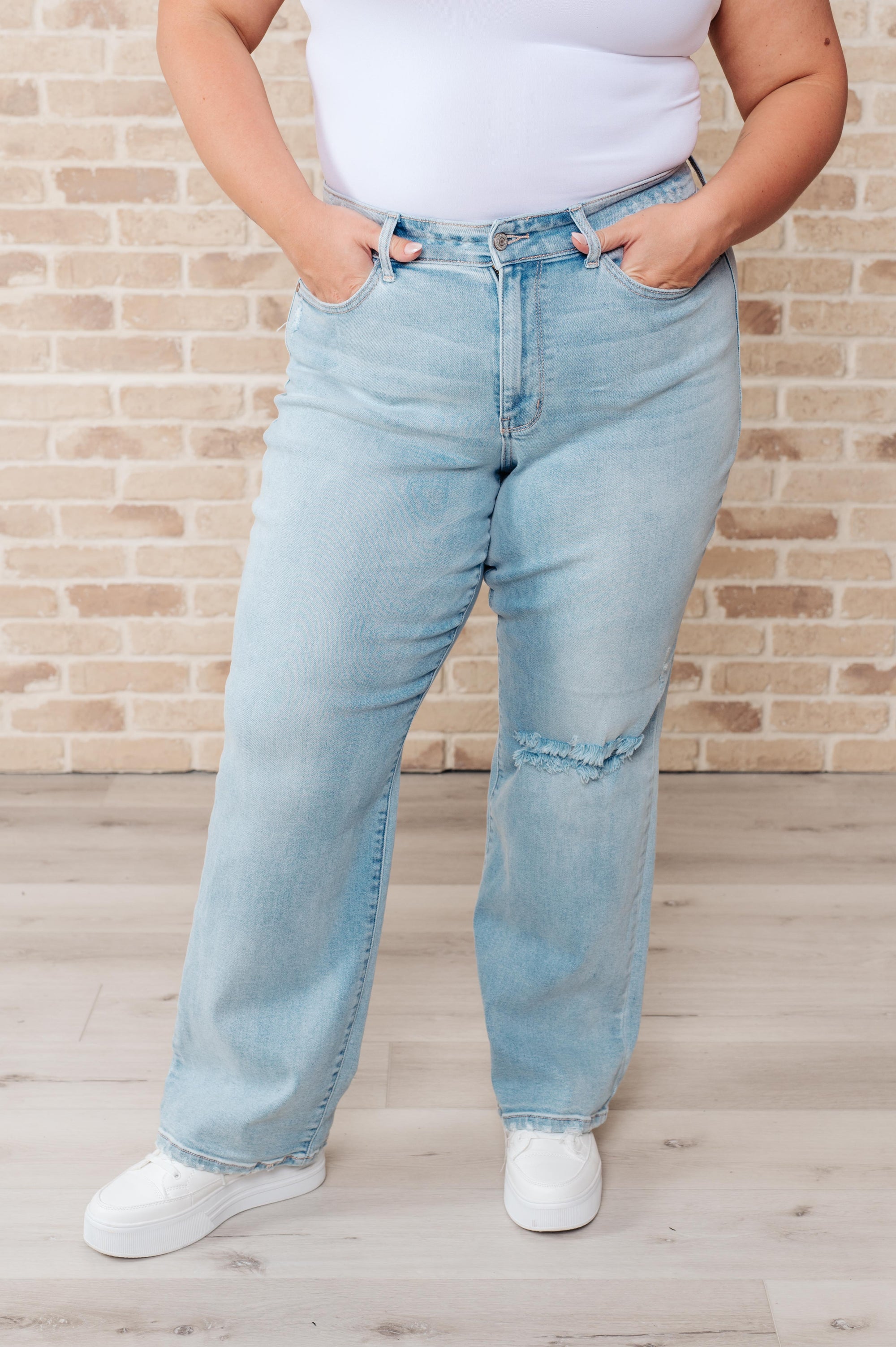 Person wearing light blue jeans and a white top against a brick wall.