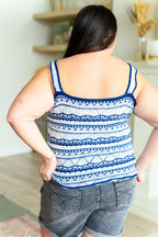 Person wearing a blue and white patterned tank top and gray shorts in a room.