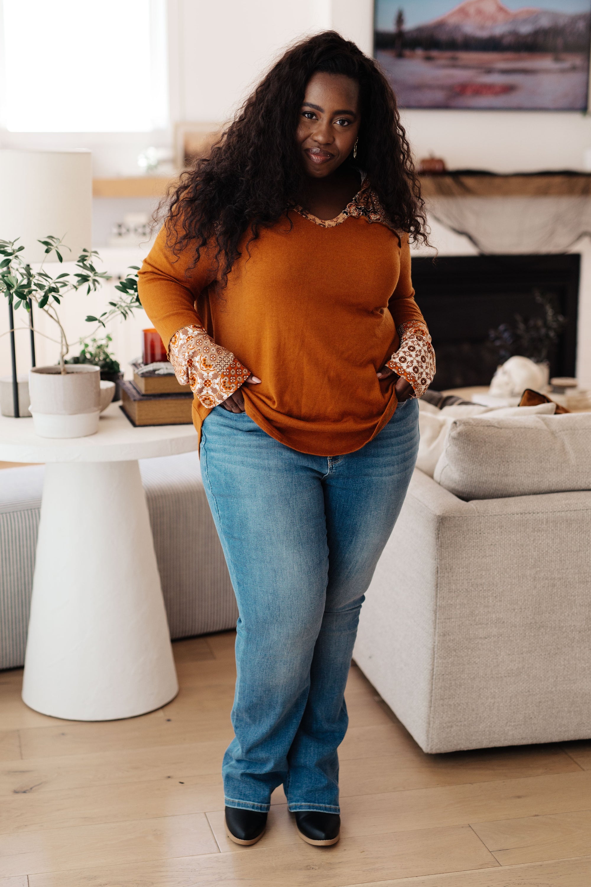 Woman in a mustard sweater and blue jeans standing in a living room.