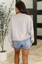 Person wearing a light gray sweatshirt and denim shorts standing indoors.