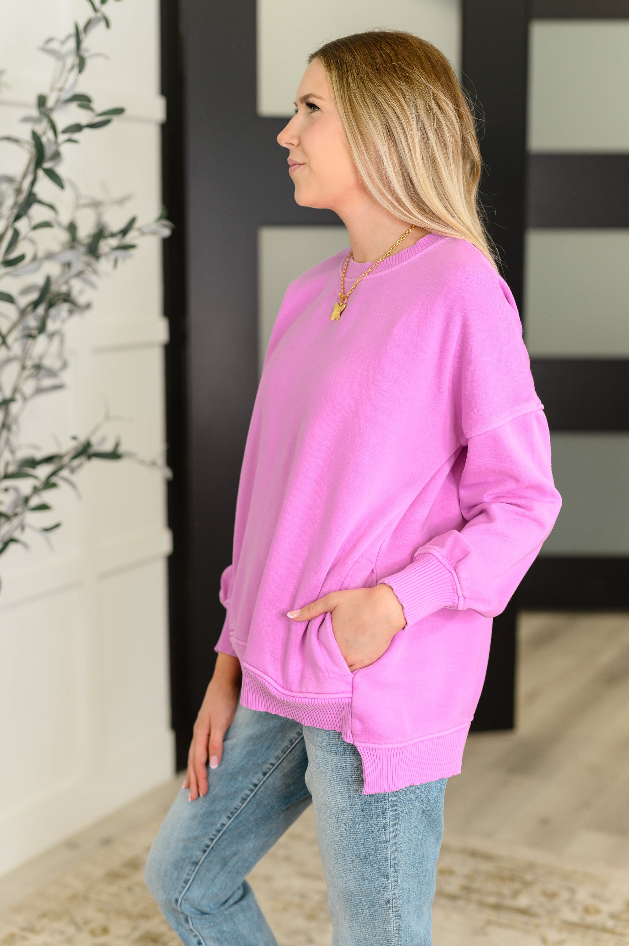 Woman wearing a pink sweatshirt and blue jeans standing indoors.