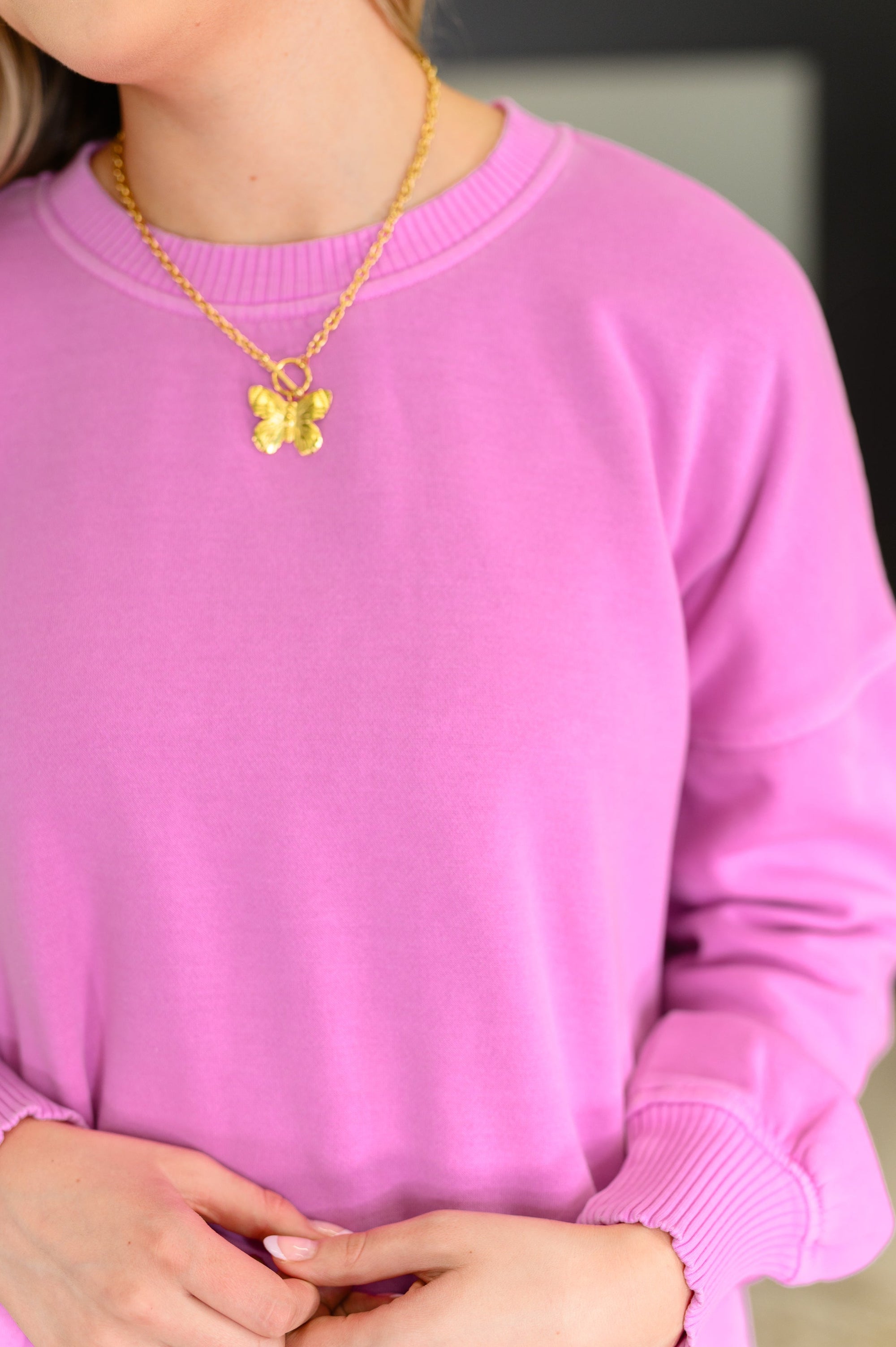 Person wearing a pink sweater and gold necklace with a butterfly pendant.