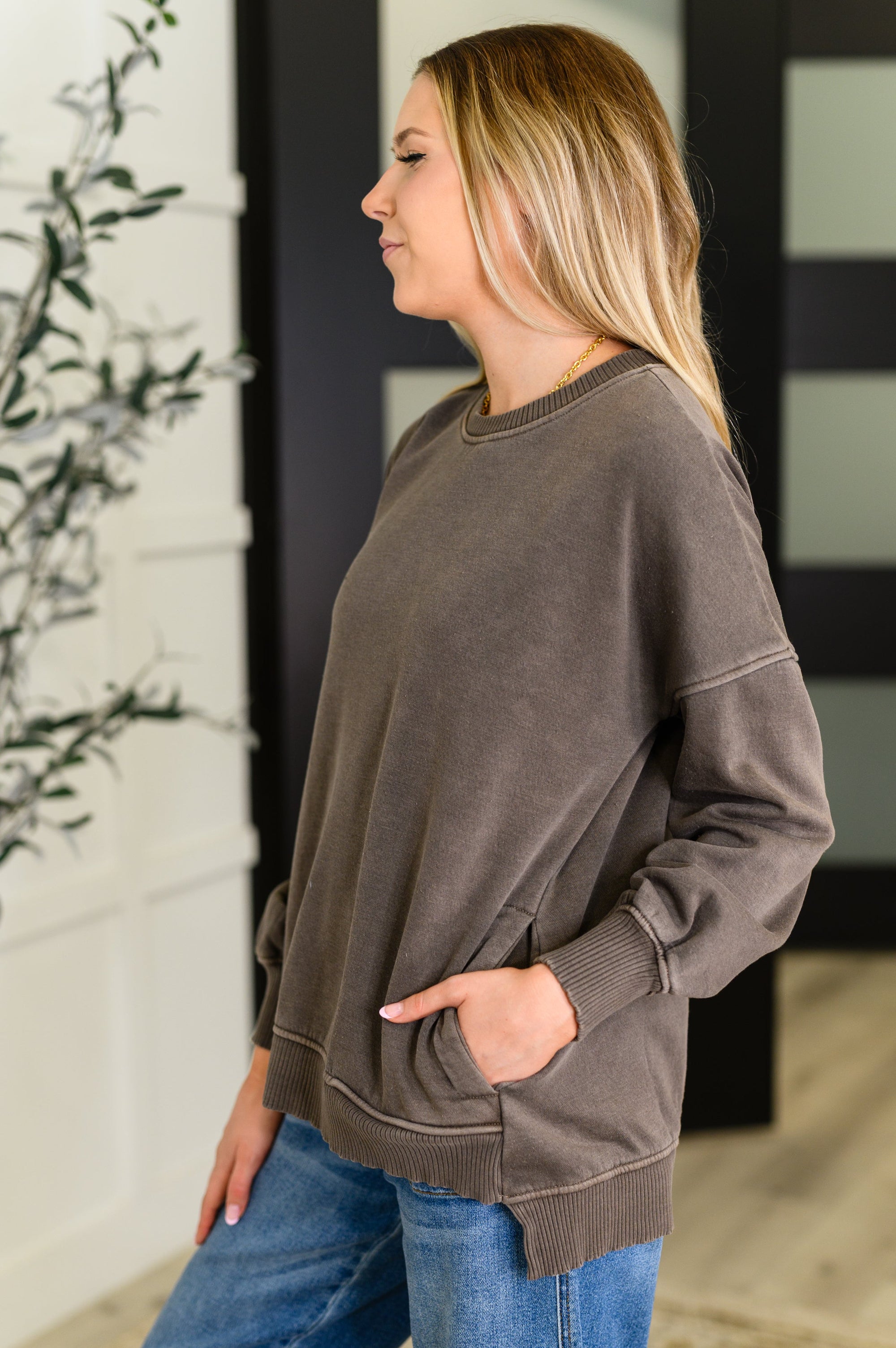 Woman wearing a brown sweatshirt and blue jeans standing indoors.