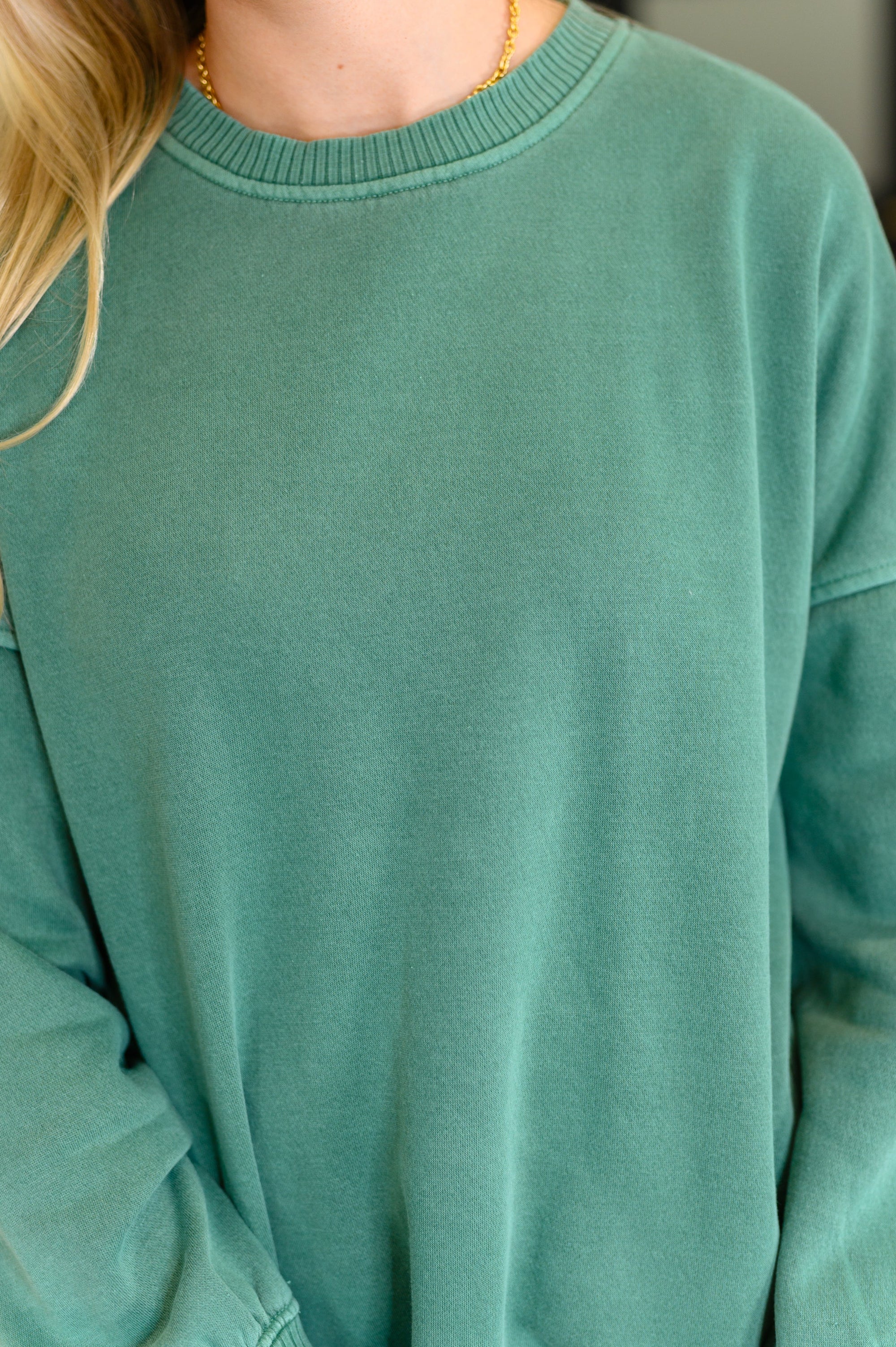 Close-up of a person wearing a teal sweater with a blurred background