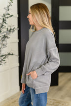 Woman wearing a gray sweatshirt and blue jeans standing outdoors.