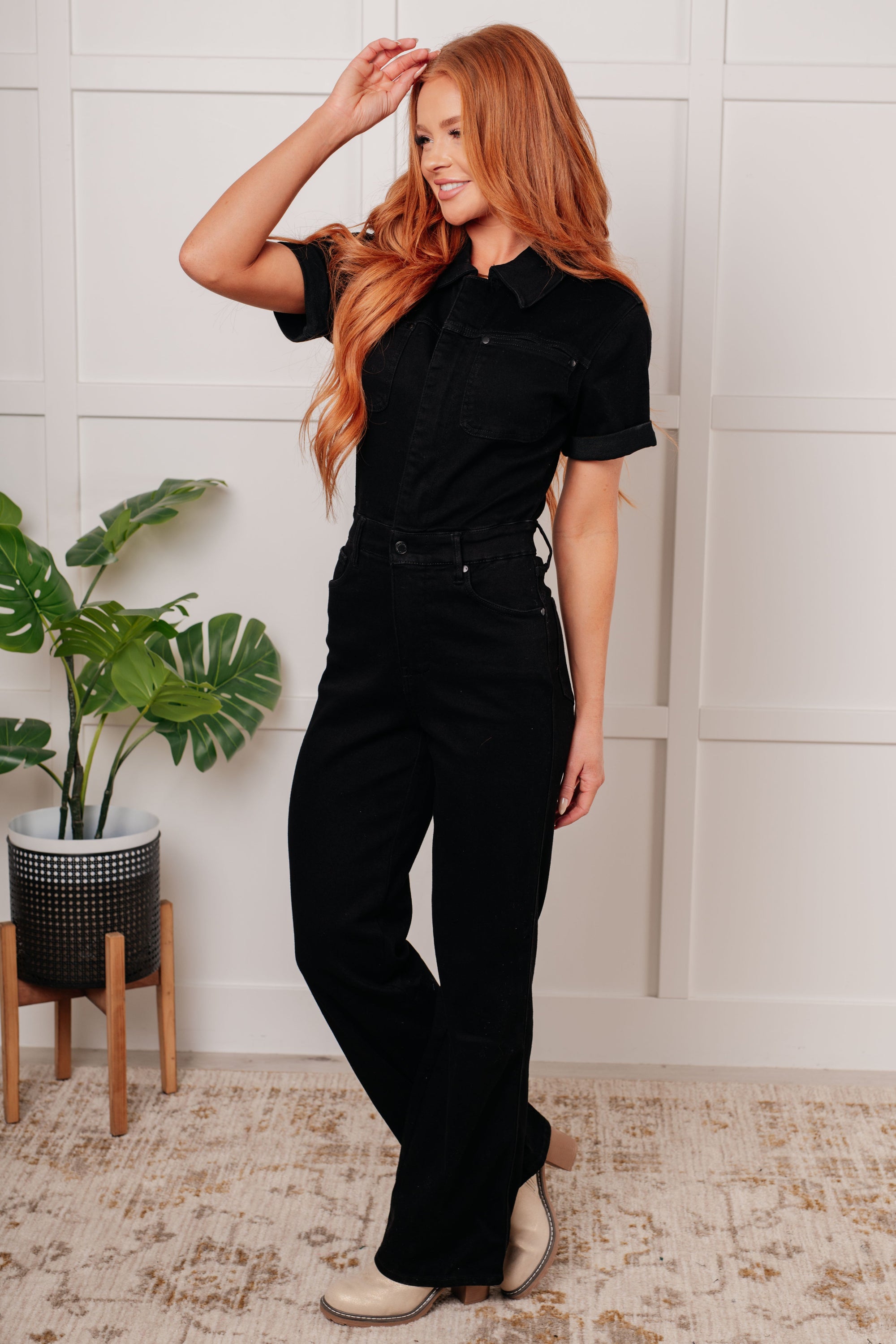 Woman wearing a black outfit standing indoors with a plant in the background
