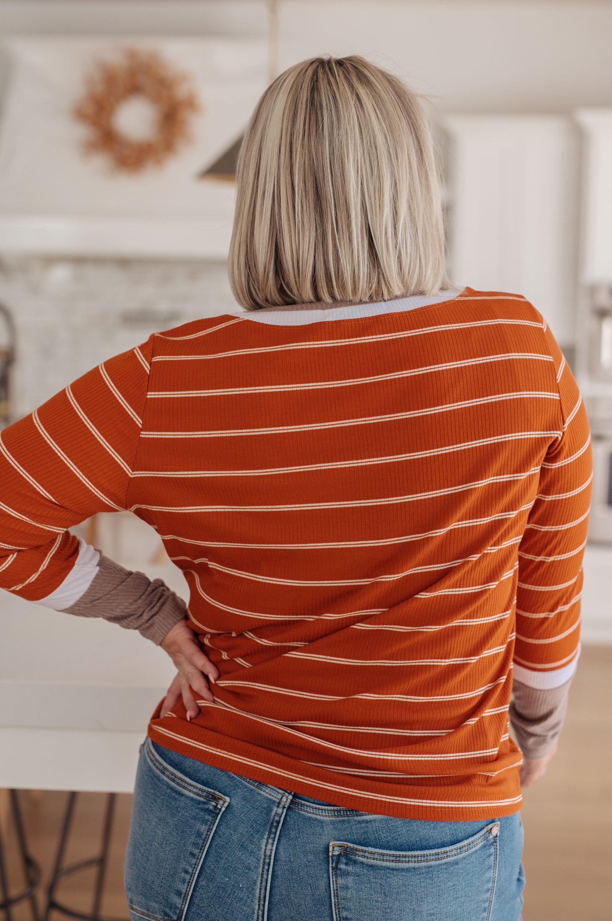 Person wearing an orange striped shirt and blue jeans in a kitchen setting