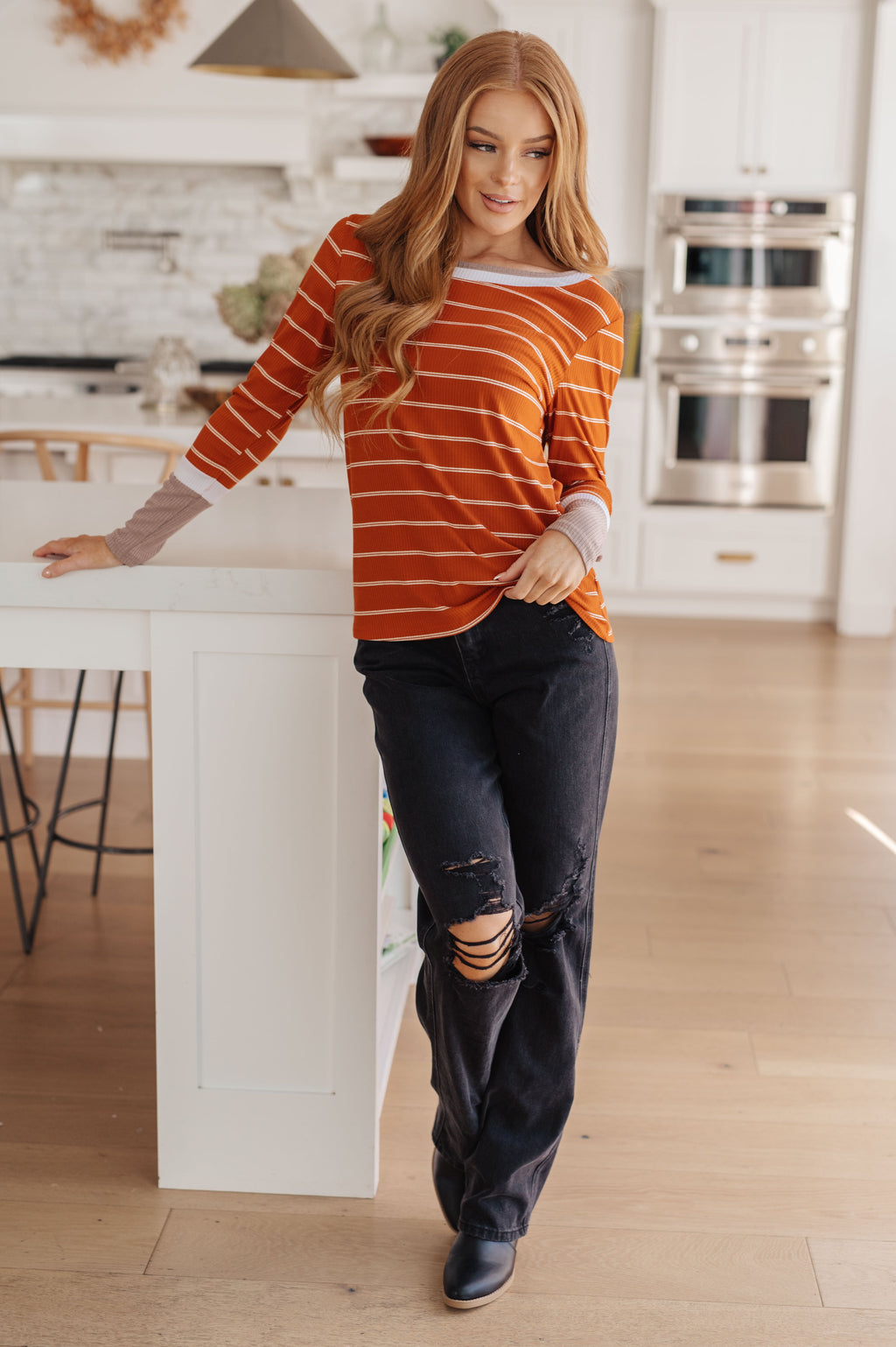 Woman in a striped sweater and jeans standing in a kitchen.