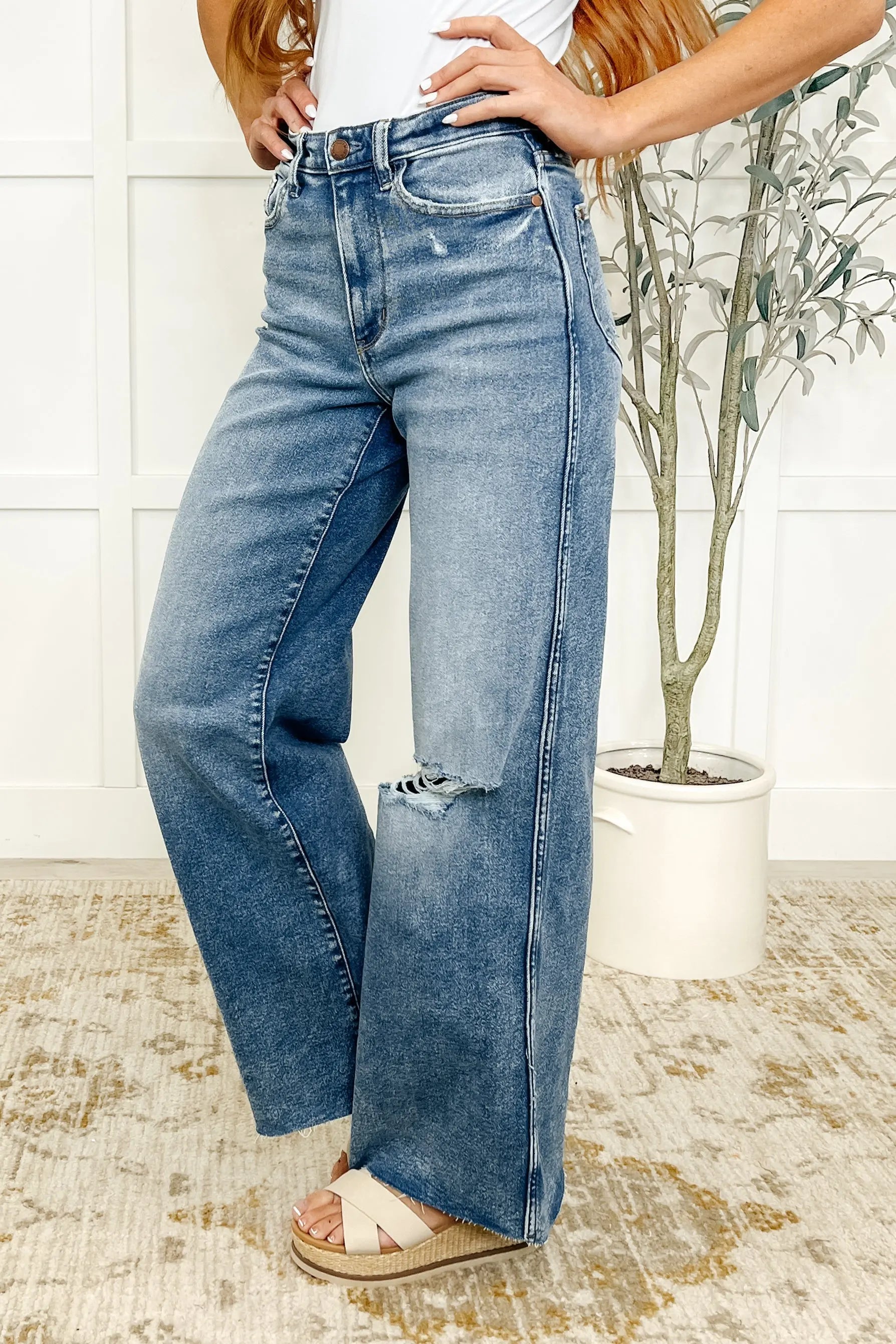 Person wearing blue jeans with a white wall and plant in the background