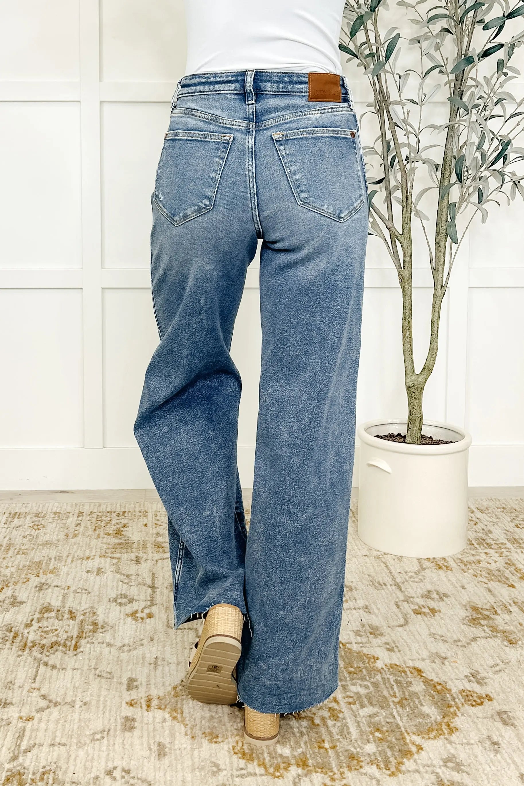 Person wearing blue jeans standing in a room with a plant and rug.